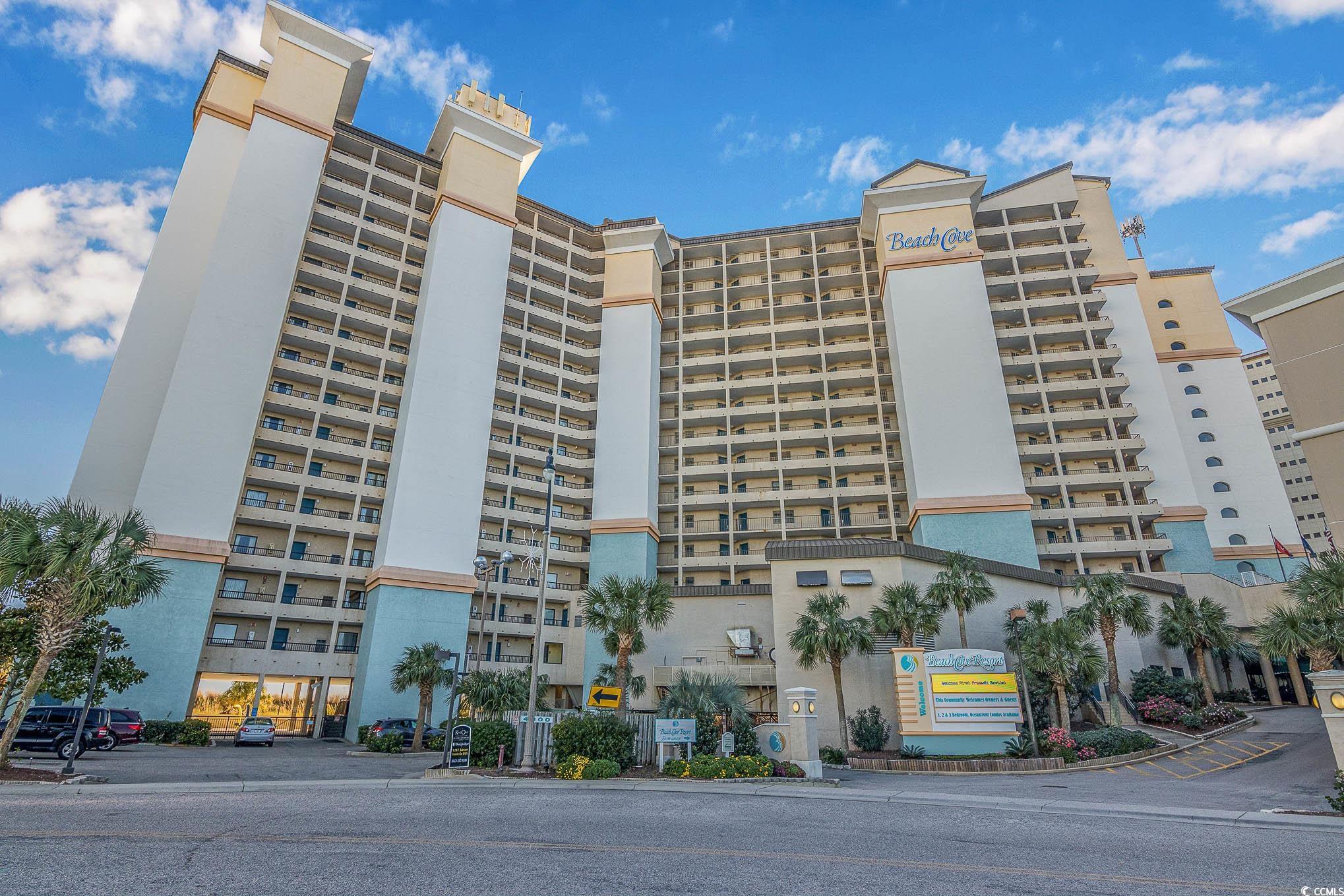 Beach Cove Resort’s high-rise exterior with rows of balconies and palm trees.