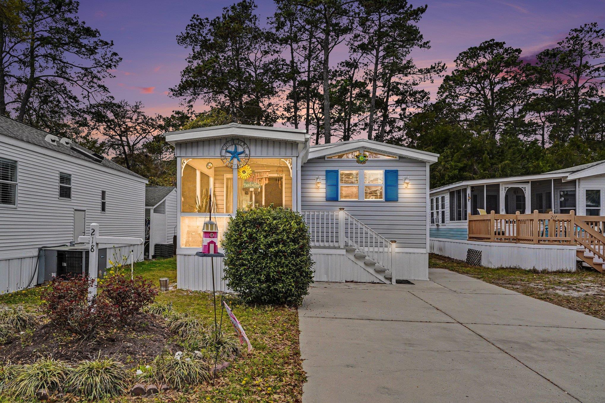 Gray home with blue shutters and a warmly lit screened porch at dusk.