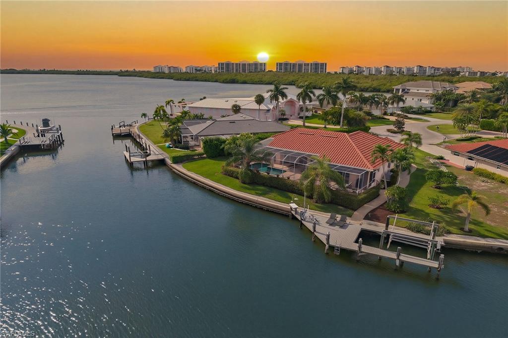 Aerial view of canal-front homes and docks beneath an orange sunset.