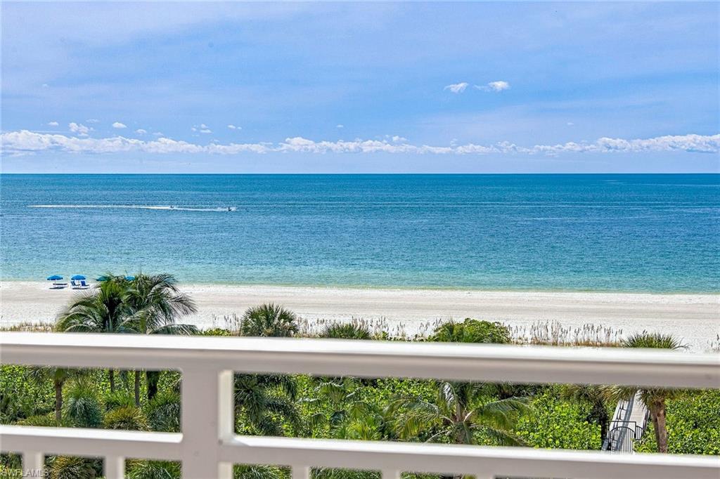 Ocean view from a balcony overlooking a sandy beach and palm-lined shore.