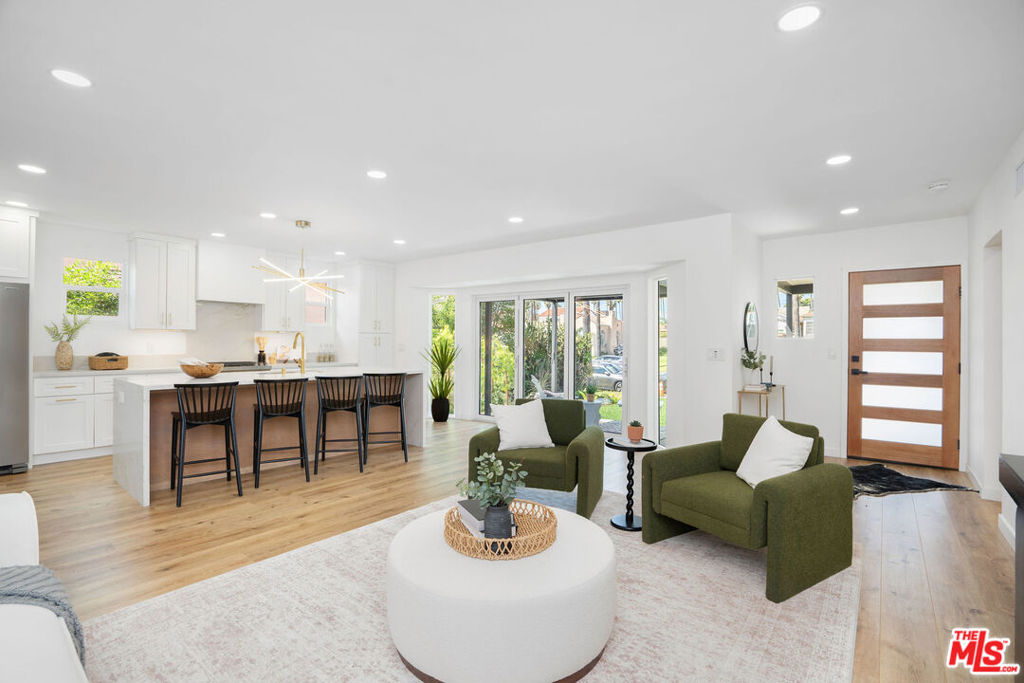 Open-plan kitchen and living room with a three-stool breakfast bar and green armchairs.