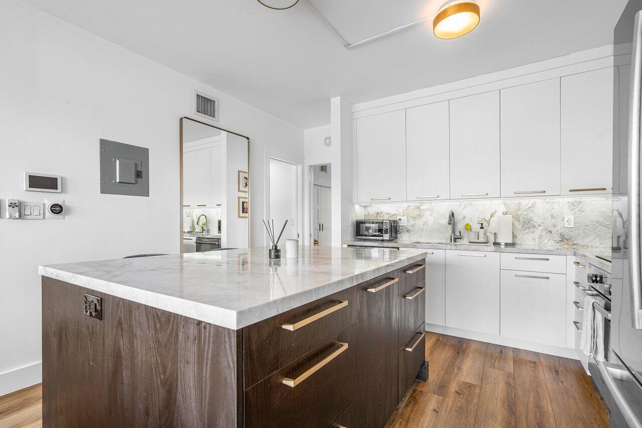 Modern kitchen with a large dark wood island, pale stone counters, white cabinets, and wood flooring.