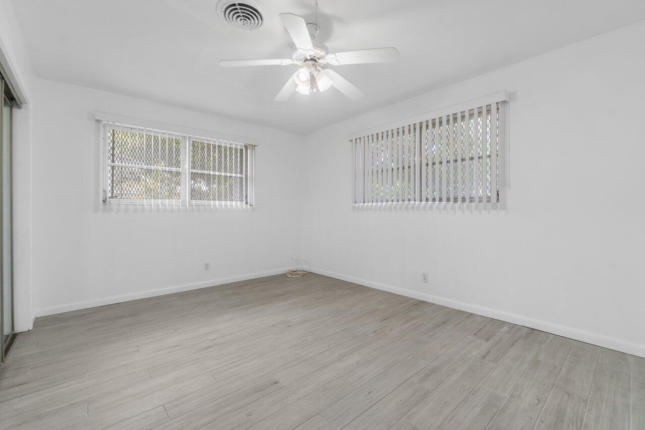 Empty room with gray tile floors, two windows with blinds, and a ceiling fan.