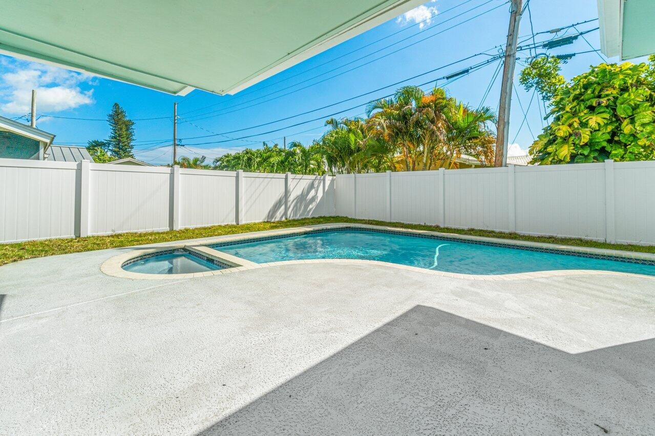 Backyard swimming pool with an attached spa, white privacy fence, and tropical trees.