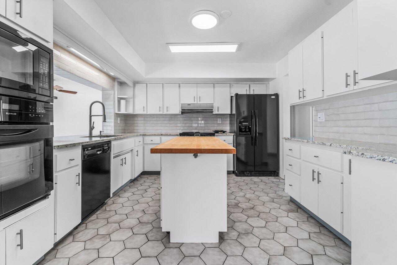 Kitchen with white cabinetry, black appliances, hexagonal tile flooring, and a butcher-block island.