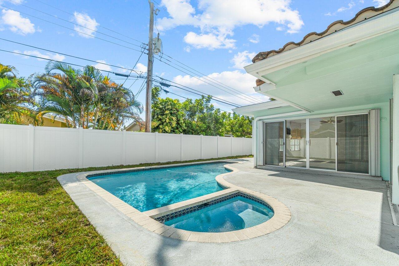 Backyard swimming pool and raised spa beside a covered patio and white privacy fence.