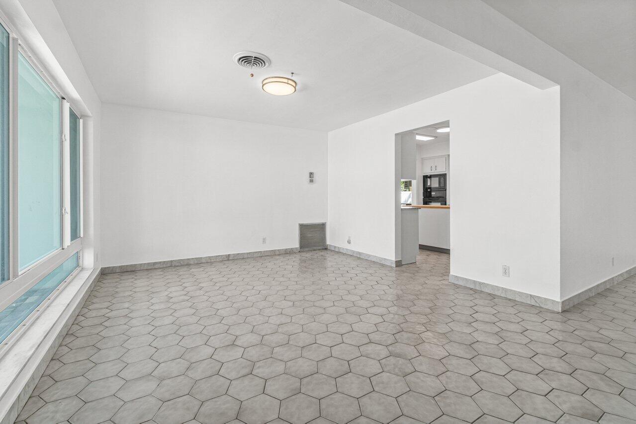 Empty tiled room with large windows and an open doorway to the kitchen.