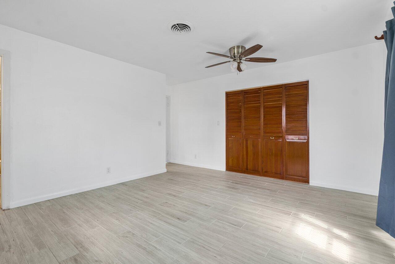 Vacant bedroom with gray tile floors, wooden louvered closet doors, and a ceiling fan.