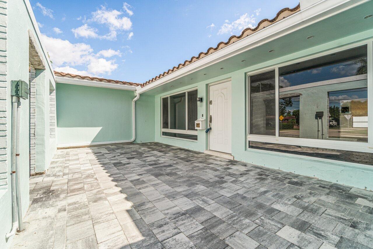 Paved courtyard patio with a covered entry, mint-green walls, and a white front door.