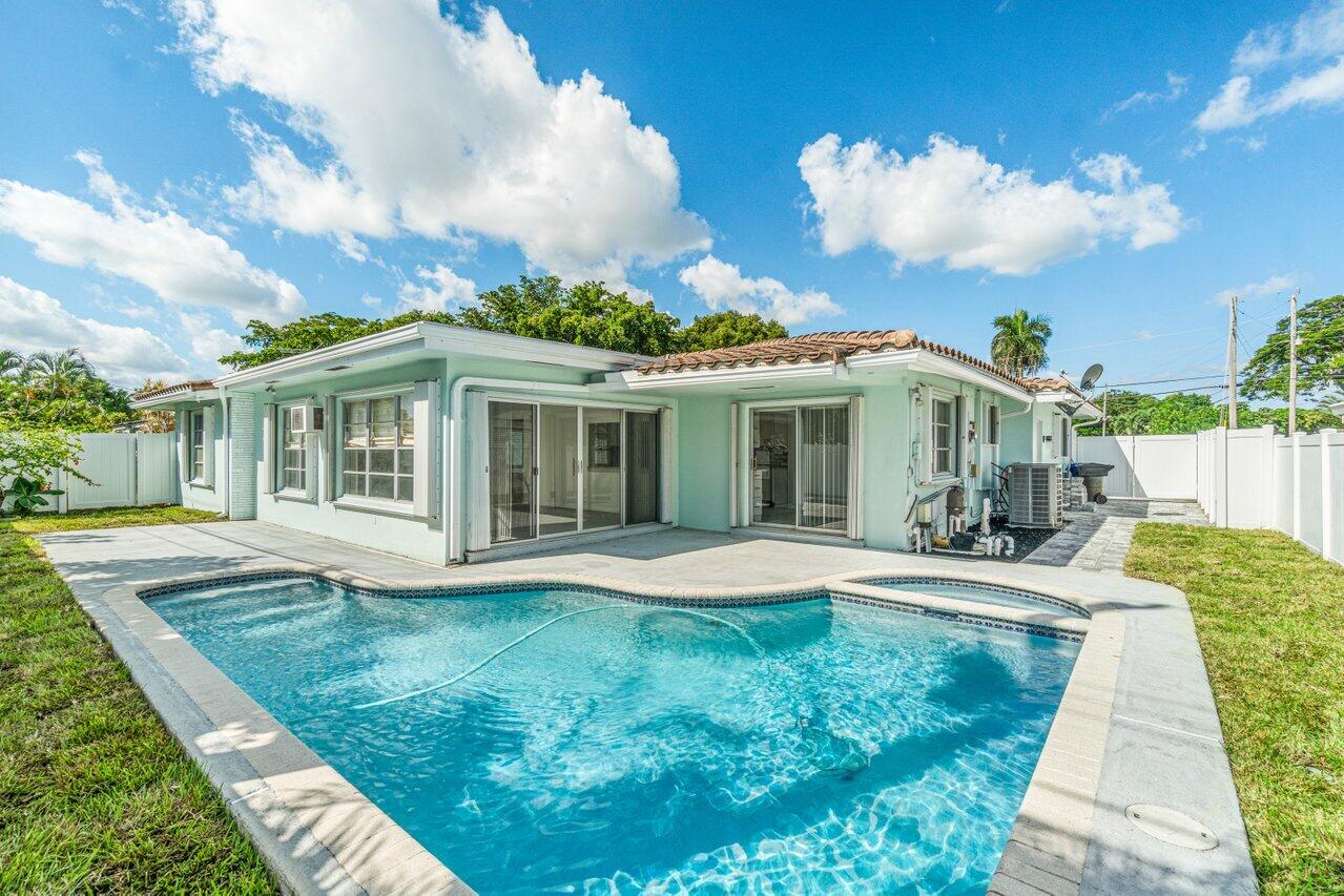 Single-story mint-green home behind a backyard pool, with a paved patio and white privacy fence.