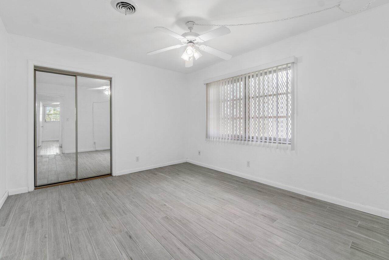 Empty bedroom with gray tile floors, mirrored closet doors, vertical blinds, and a ceiling fan.