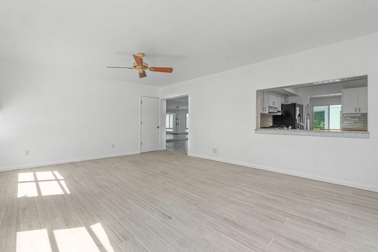 Vacant living room with light gray tile flooring, a ceiling fan, and a kitchen pass-through.