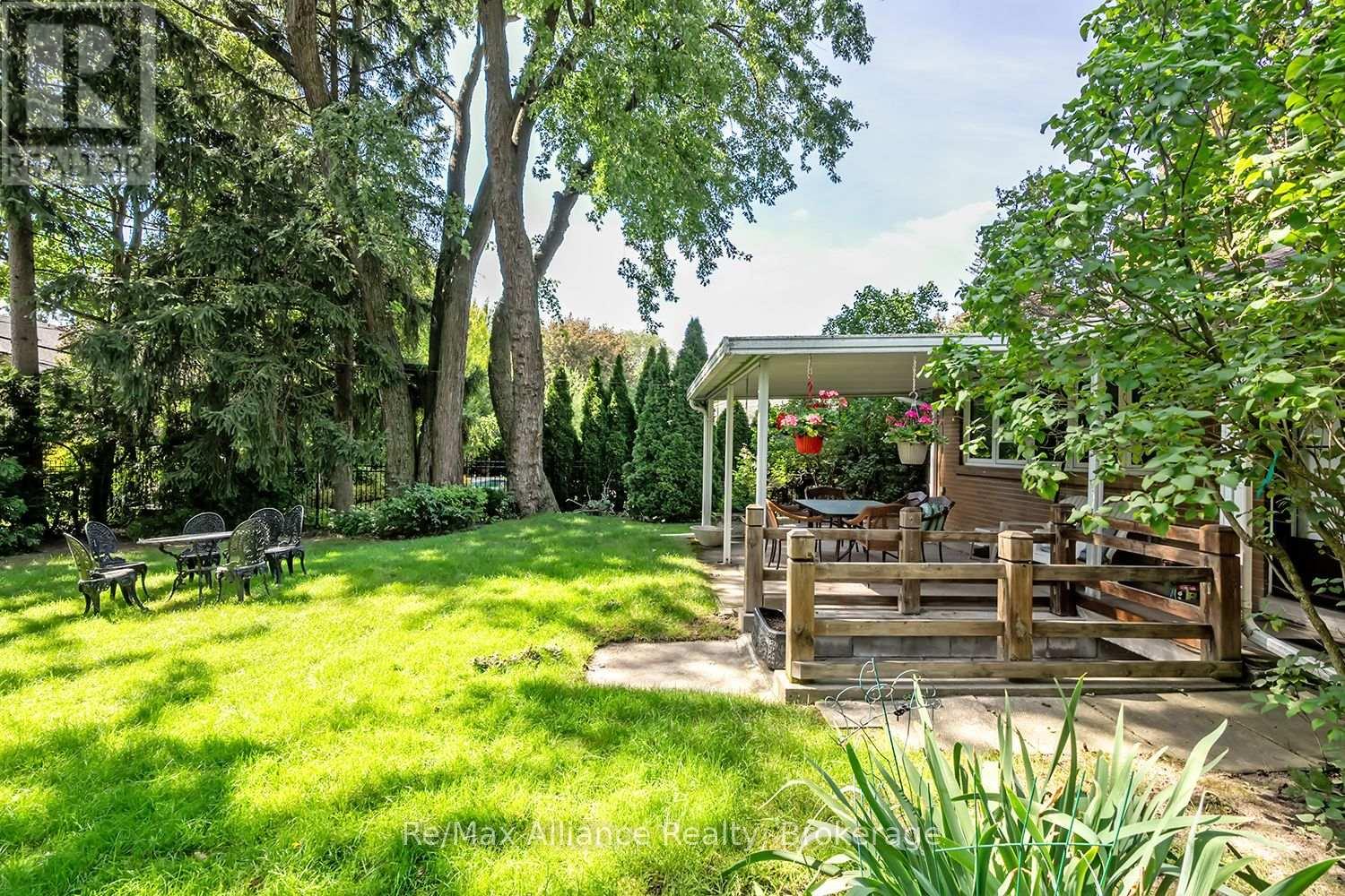 Shaded backyard with a broad lawn, mature trees, and a covered patio with outdoor seating.