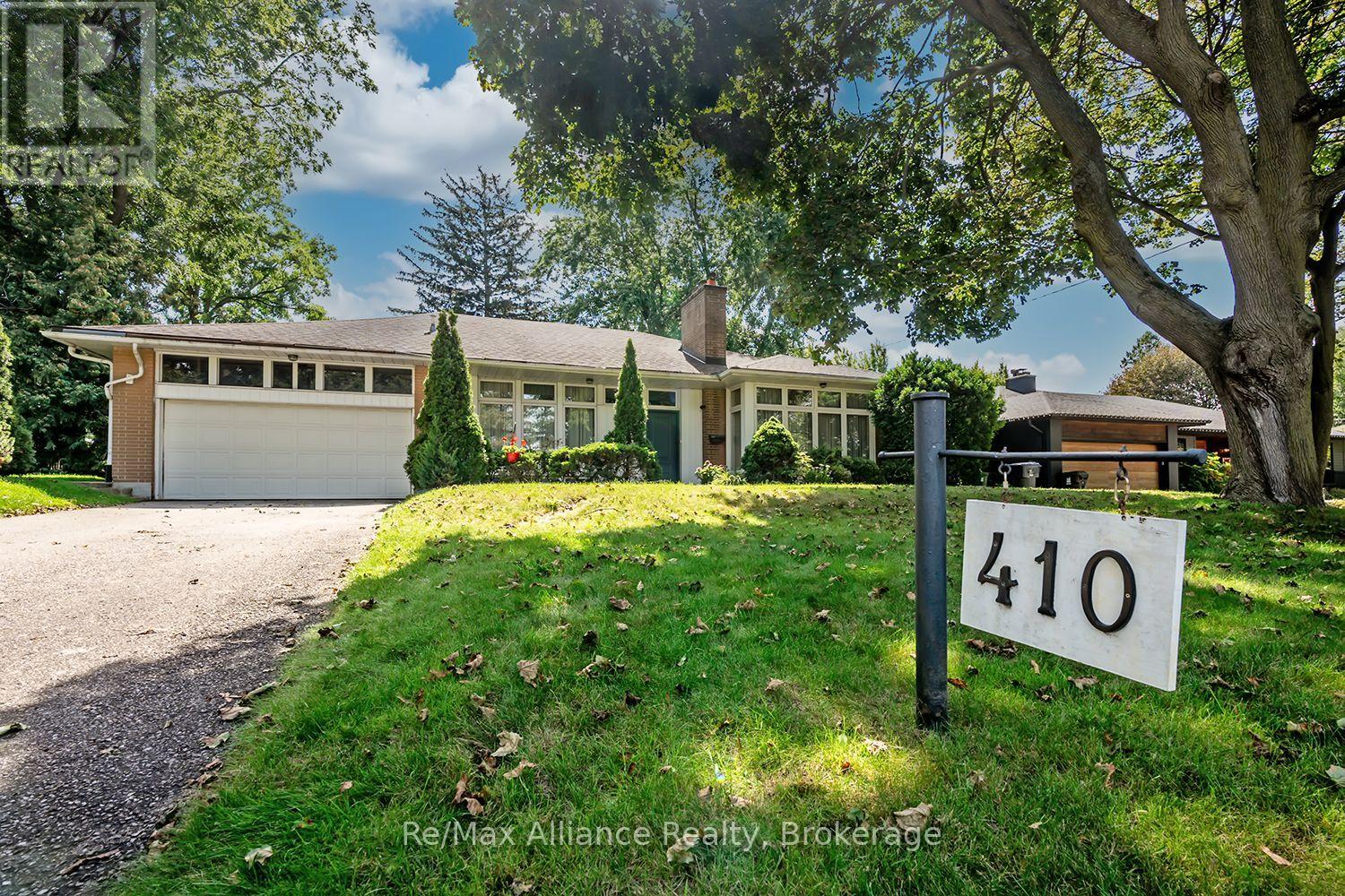 Single-story home with an attached double garage, broad front windows, mature trees, and a sloping lawn.