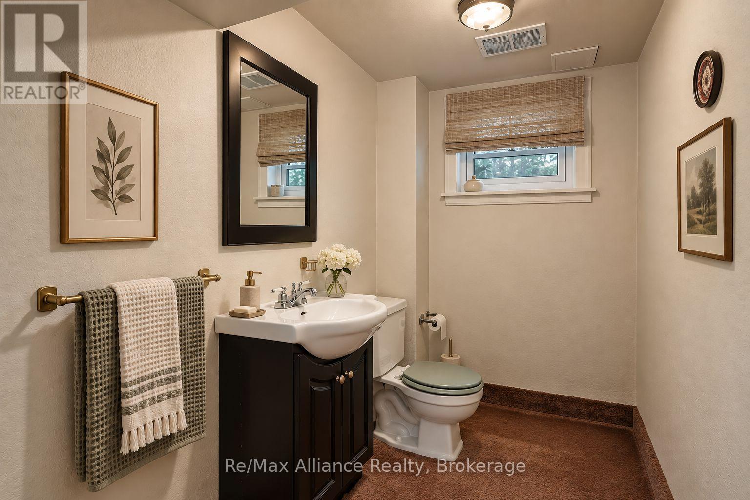 Bathroom with a dark vanity, white sink and toilet, woven blinds, and framed botanical art.