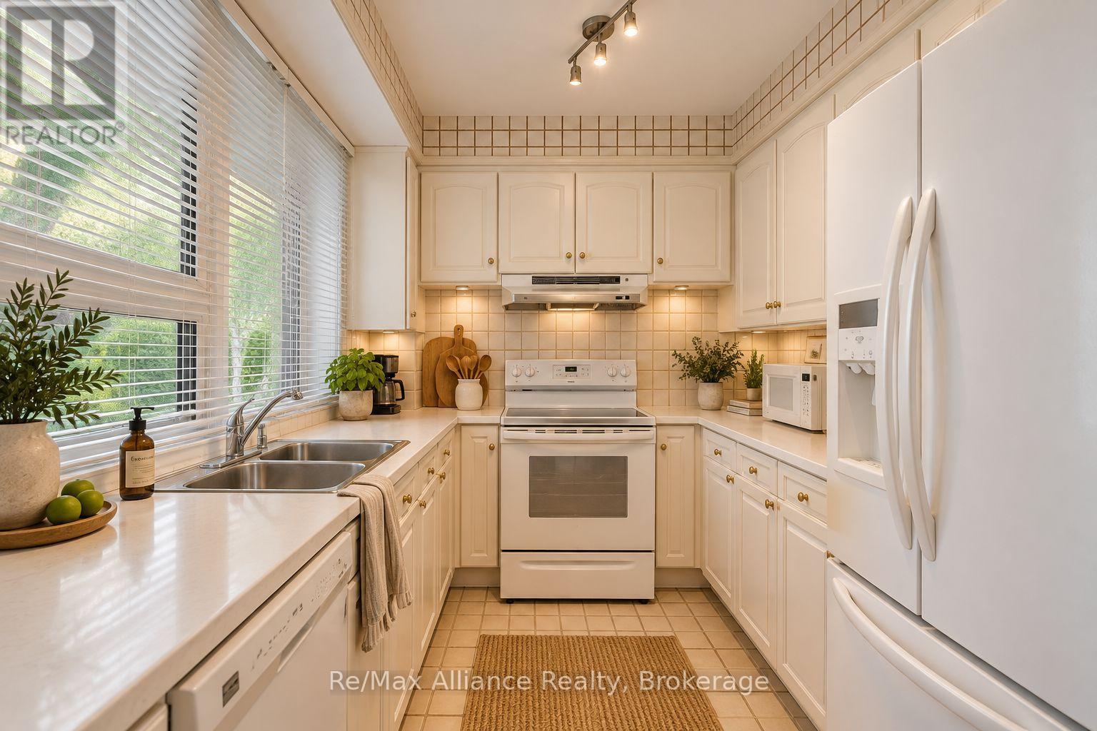 Cream kitchen with white appliances, a double sink, and a large window with blinds.