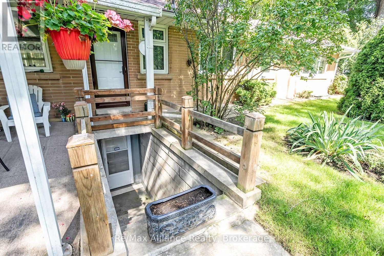 Brick home porch with a sunken stairwell entrance, wooden railing, and hanging flower baskets.