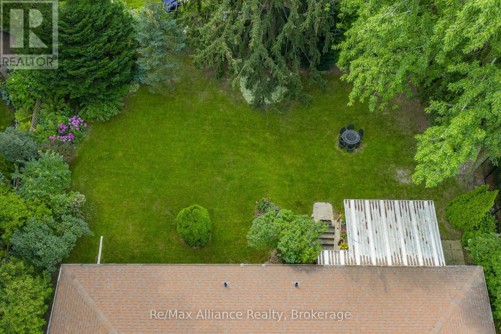 Aerial view of a spacious tree-lined backyard with a broad lawn, patio table, and deck.