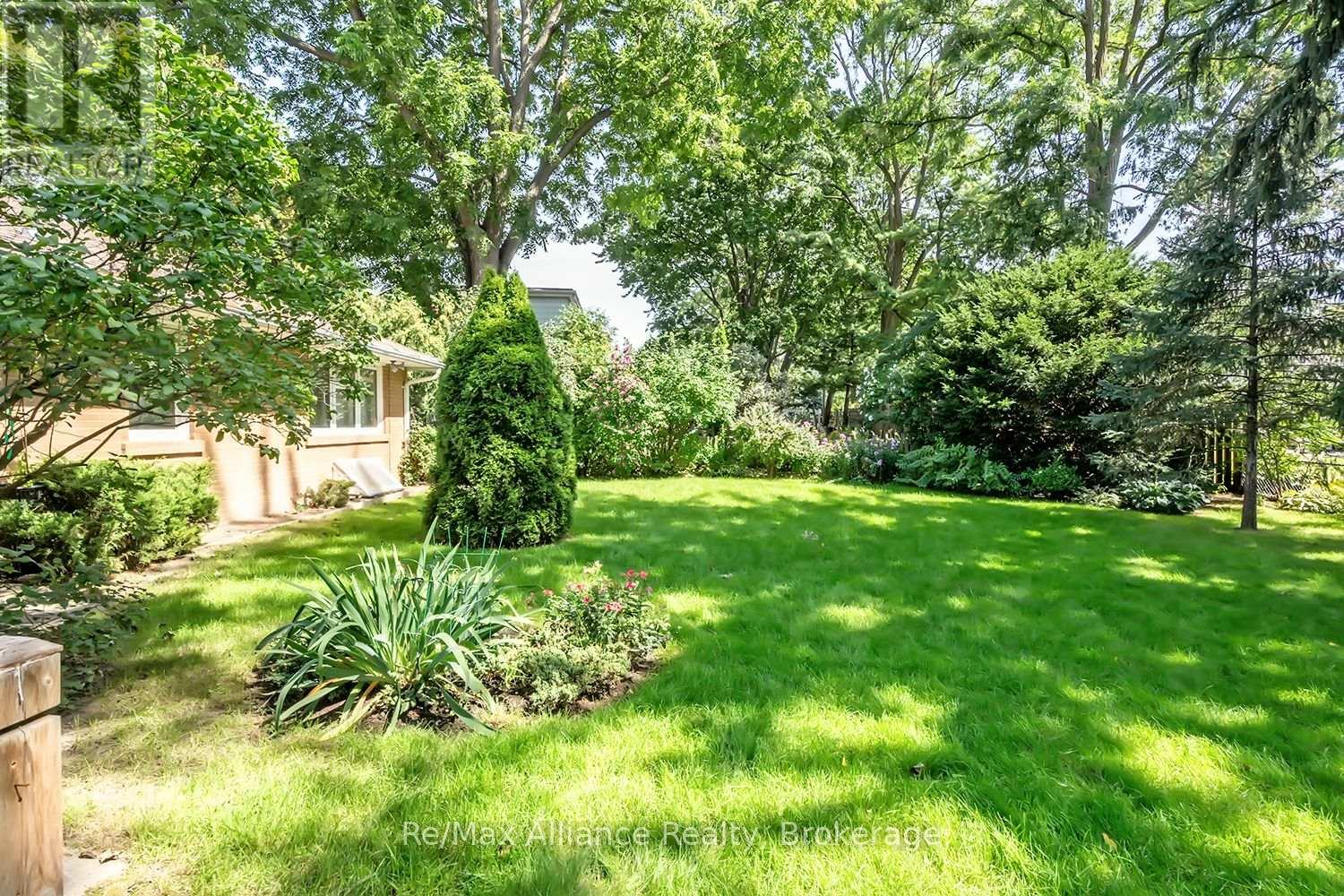 Landscaped backyard with a broad lawn, mature trees, flower beds, and the house at left.