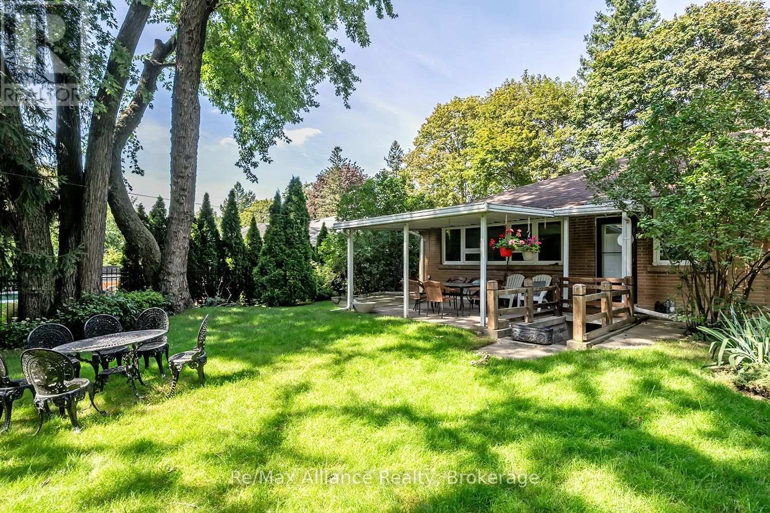 Brick home with a covered patio overlooking a broad lawn shaded by mature trees.