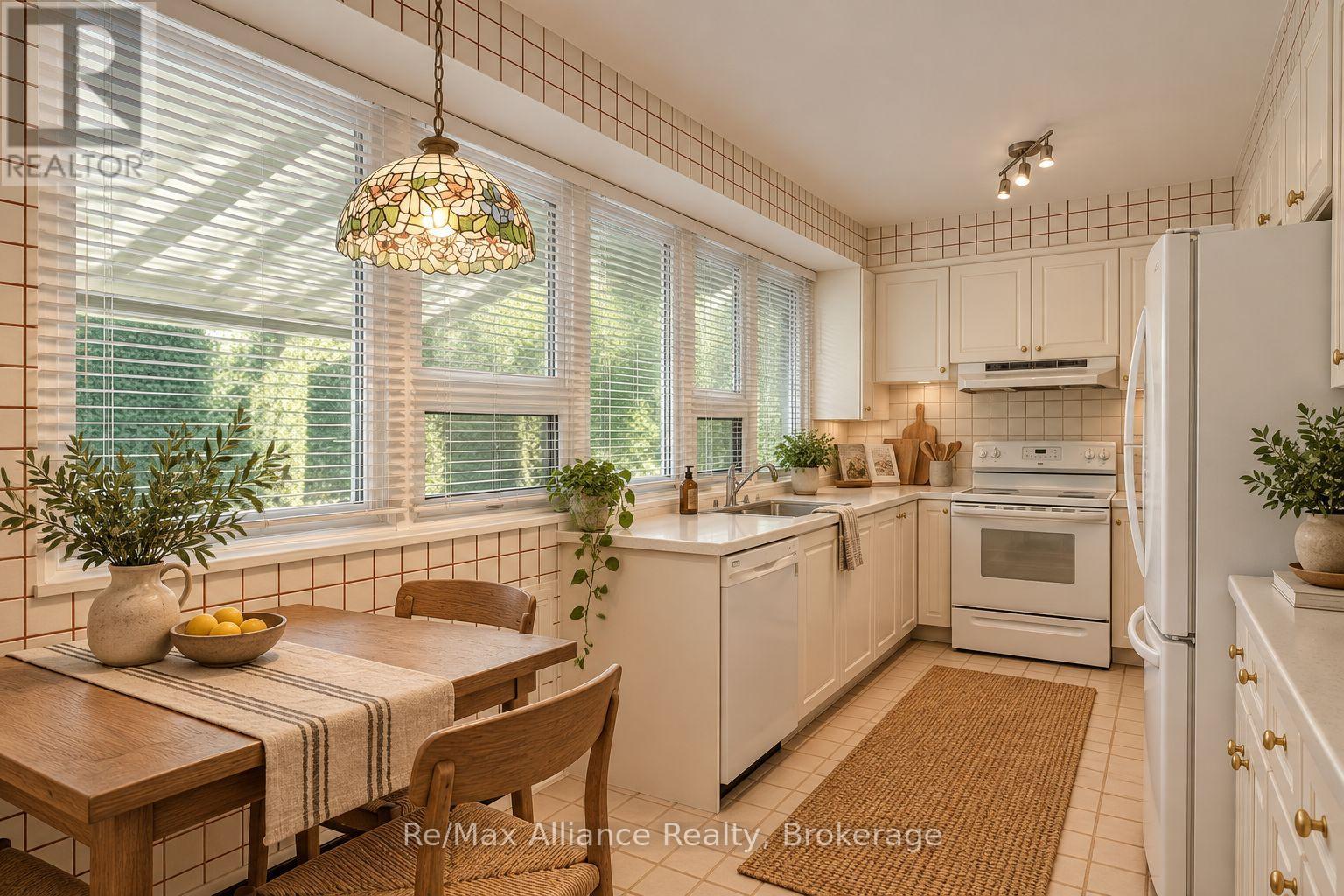 Bright kitchen with white cabinetry, expansive windows, and a wooden dining table beneath a stained-glass pendant.