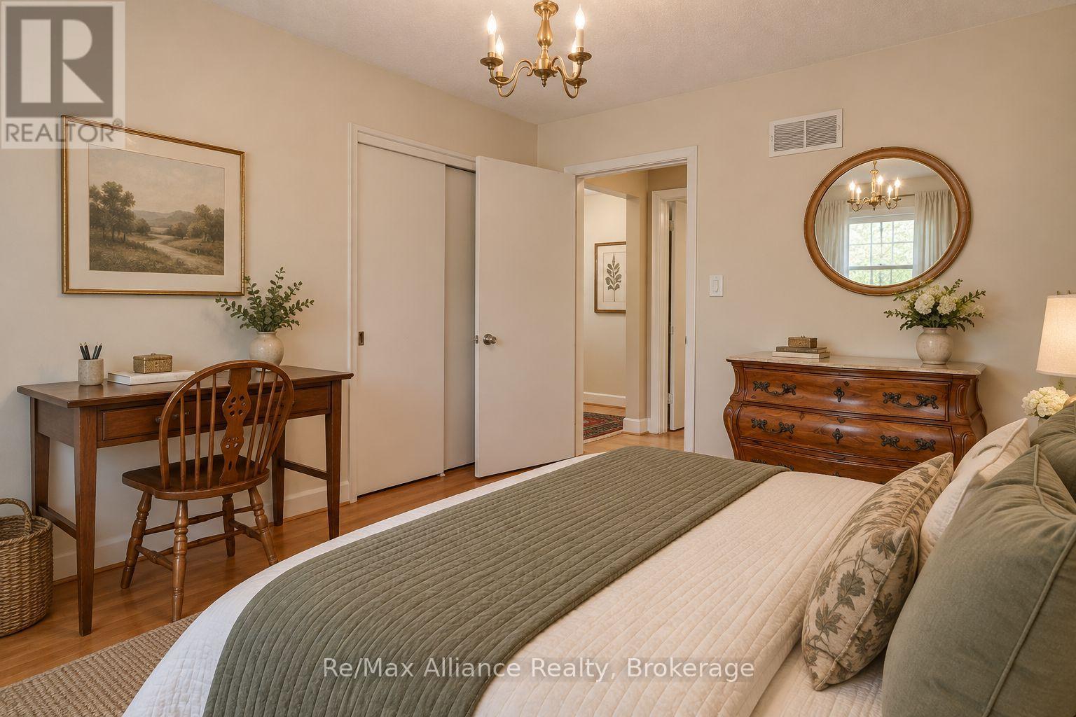 Furnished bedroom with sage bedding, a wooden desk and chair, an ornate dresser, and a brass chandelier.