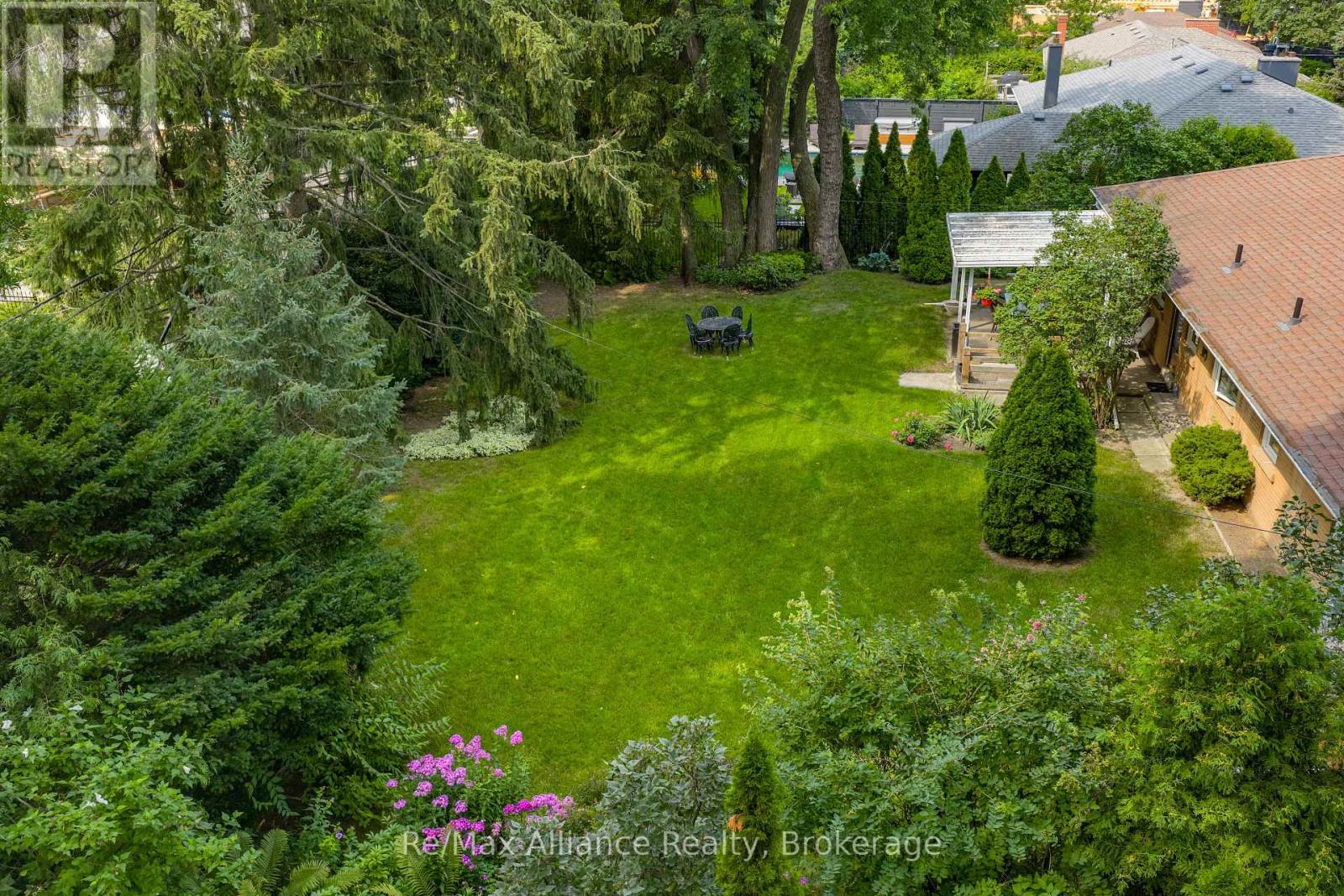 Spacious backyard with a broad lawn, mature evergreens, and a small patio dining set.