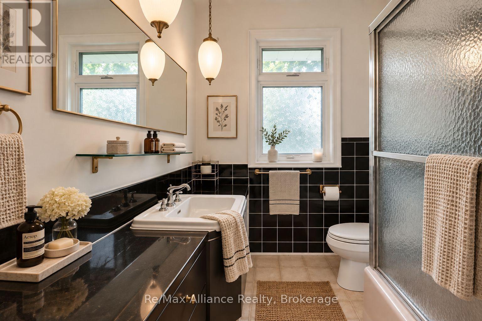 Bathroom with a glossy black vanity, black tile wainscoting, and a glass shower enclosure.