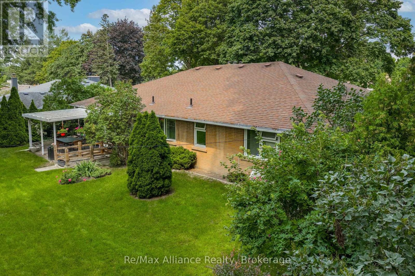Rear of a brick bungalow with a covered patio, wood deck, and leafy landscaped garden.