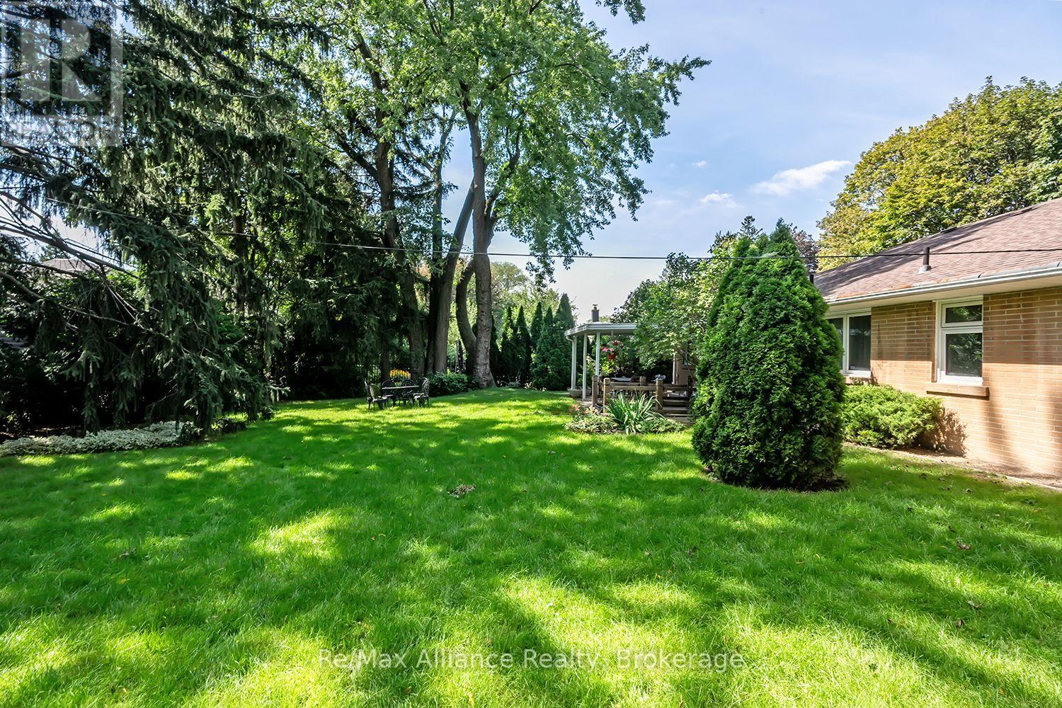 Spacious backyard with a broad lawn, mature trees, and a covered patio beside a brick home.