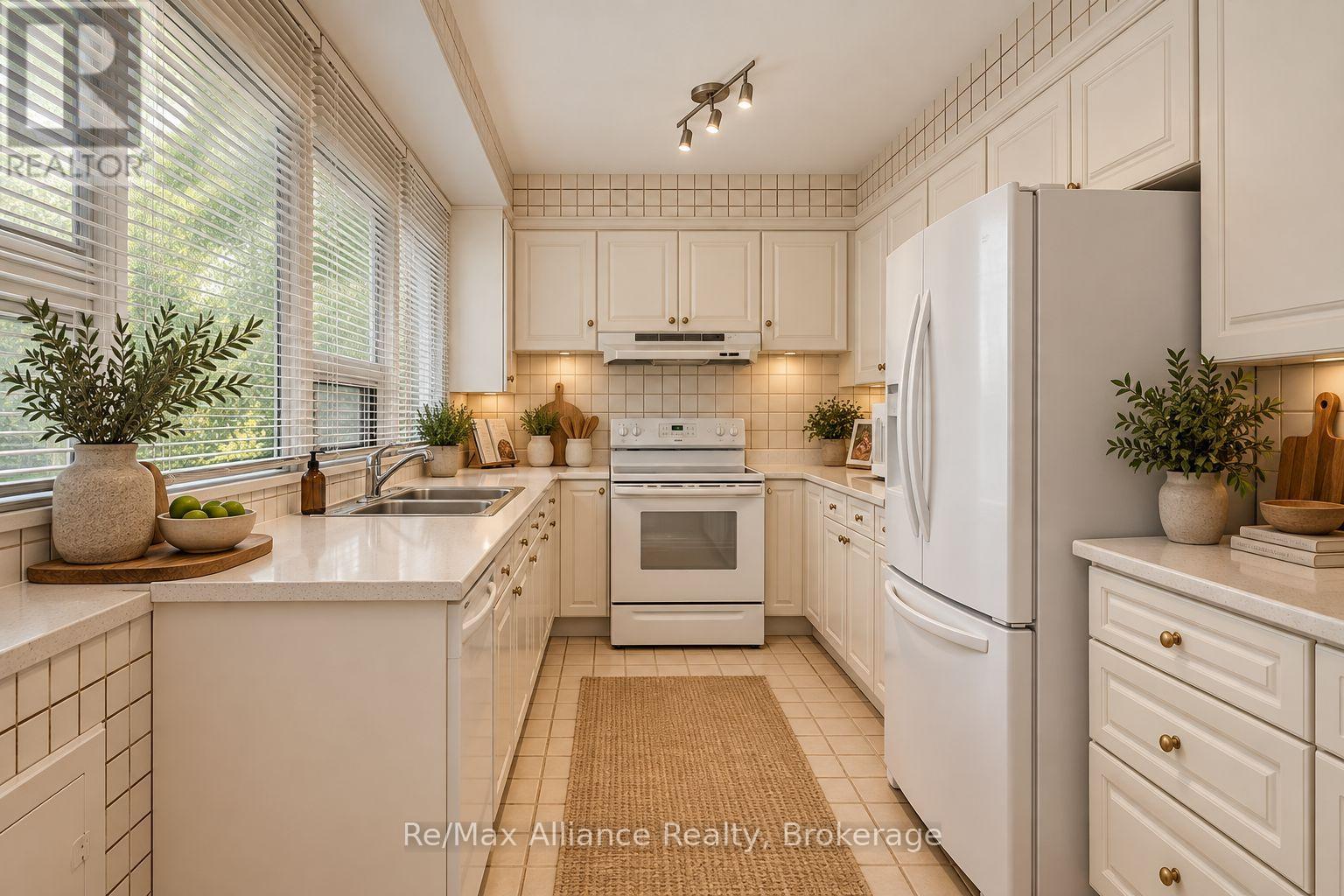 Bright cream kitchen with white appliances, tiled backsplash, and a wide window above the sink.