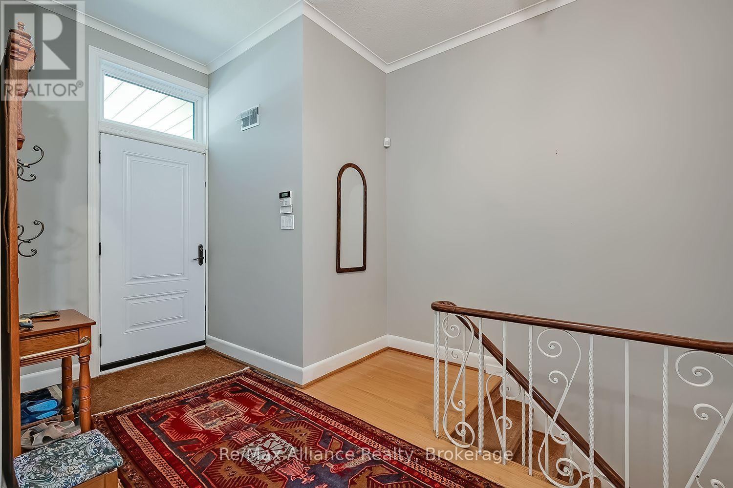 Entry foyer with a white front door, patterned rug, and decorative railing beside the staircase.