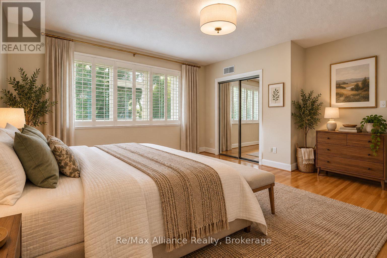 Staged bedroom with plantation shutters, mirrored closet doors, and a large bed with a textured throw.