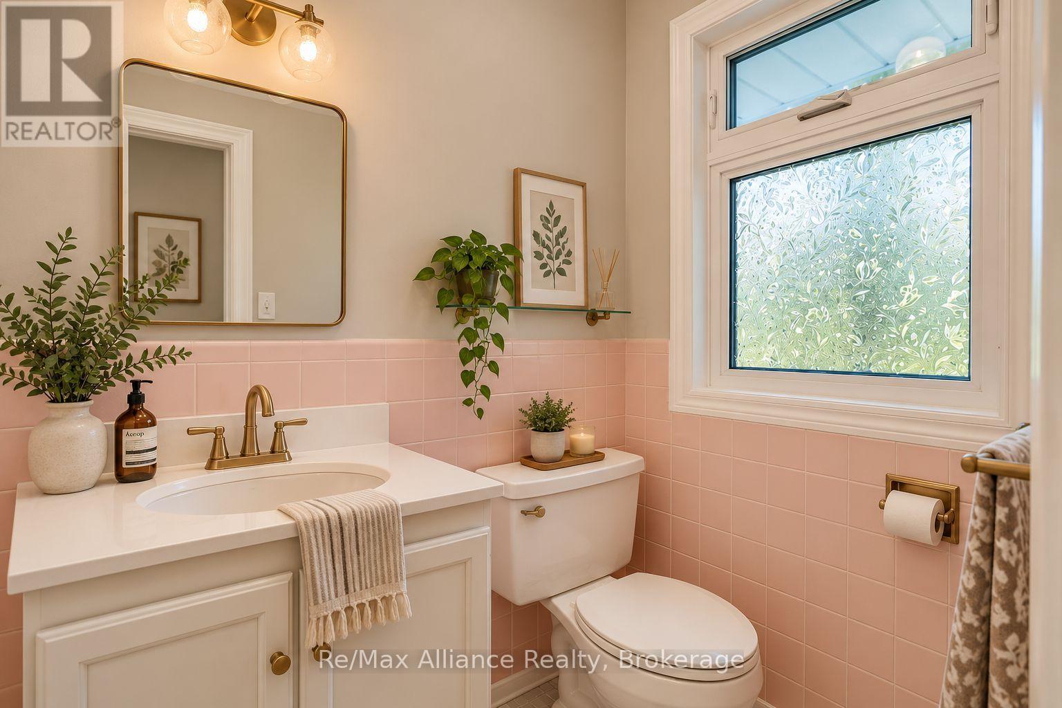Bathroom with pink tile, a white vanity, brass fixtures, and a large patterned privacy window.