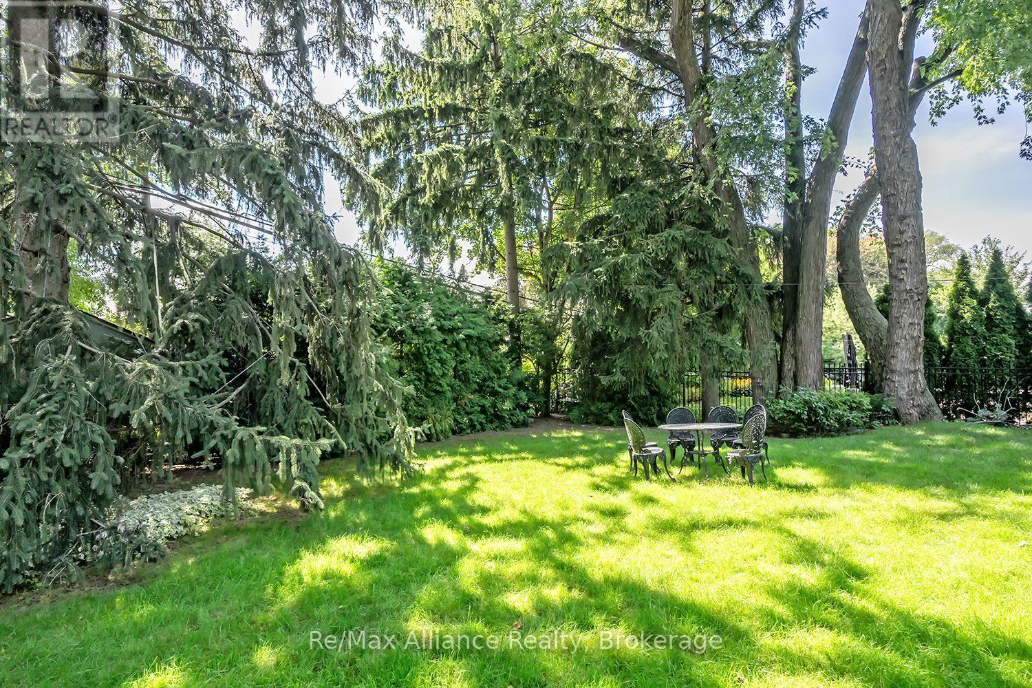 Landscaped backyard with mature trees, a sunny lawn, and a small outdoor dining set.