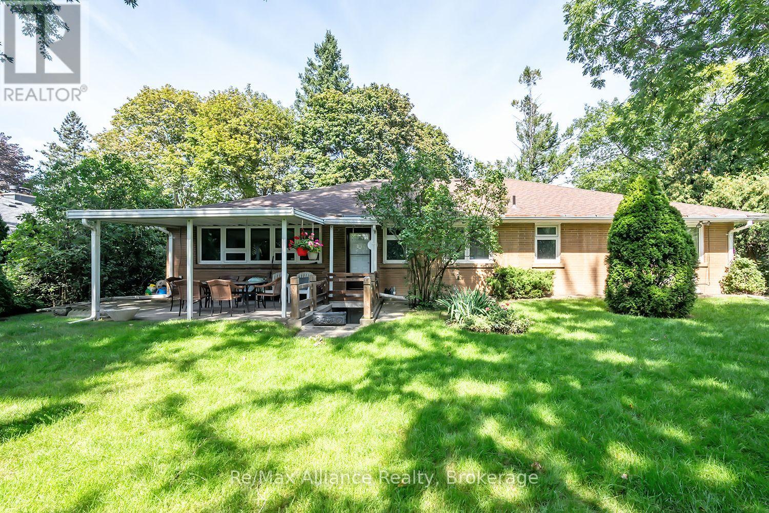 Rear of a brick home with a covered patio, outdoor dining furniture, and a spacious green lawn.
