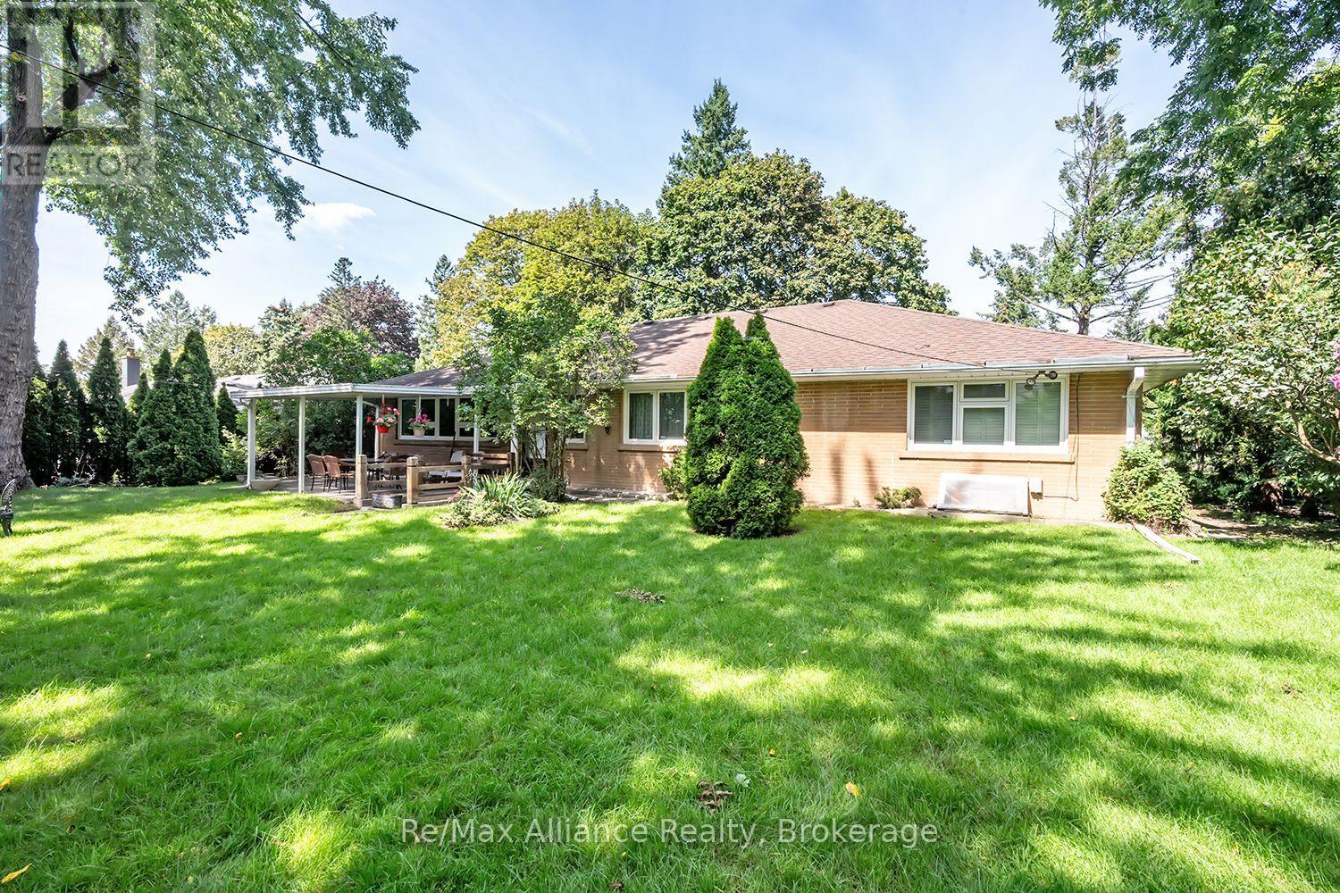 Rear of a brick house with a covered patio, mature trees, and a broad green lawn.