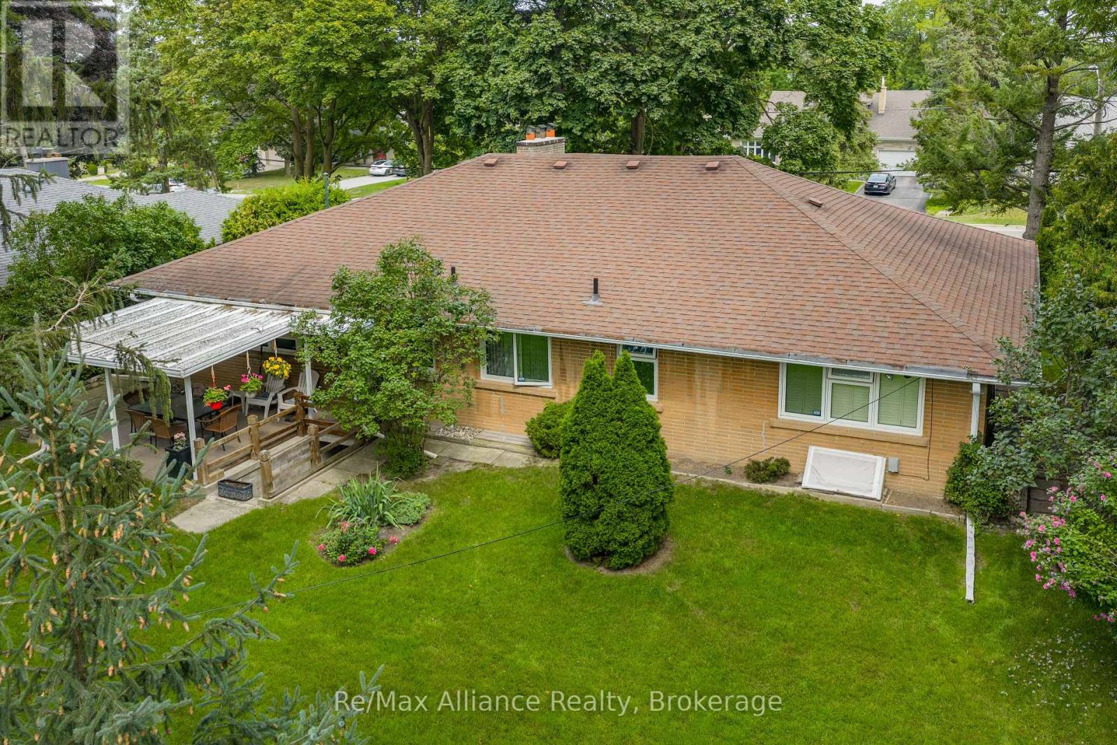 Rear of a brick house with a broad brown roof, leafy yard, and covered patio.