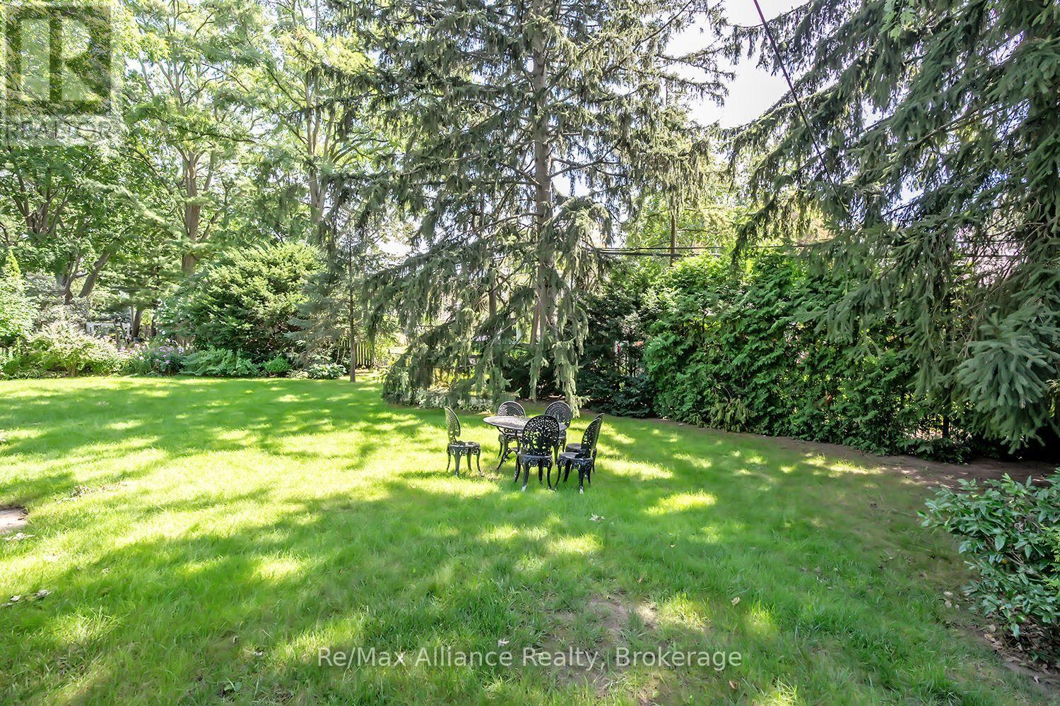 Shaded backyard lawn with patio table and chairs beneath mature trees.