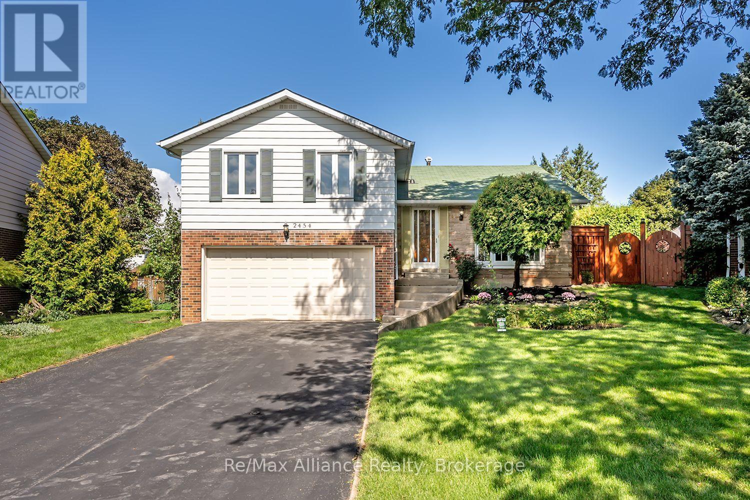 Two-storey house with an attached double garage, wide driveway, landscaped garden, and wooden side gate.