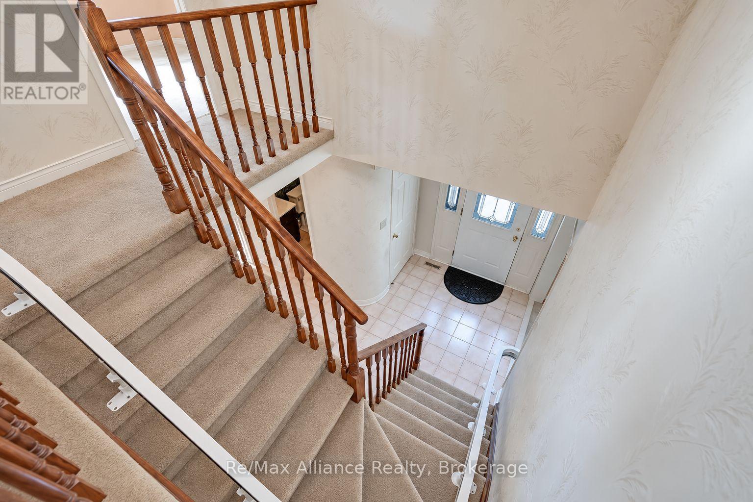 Carpeted staircase with wooden railings overlooking a tiled foyer and glass-paneled front door.