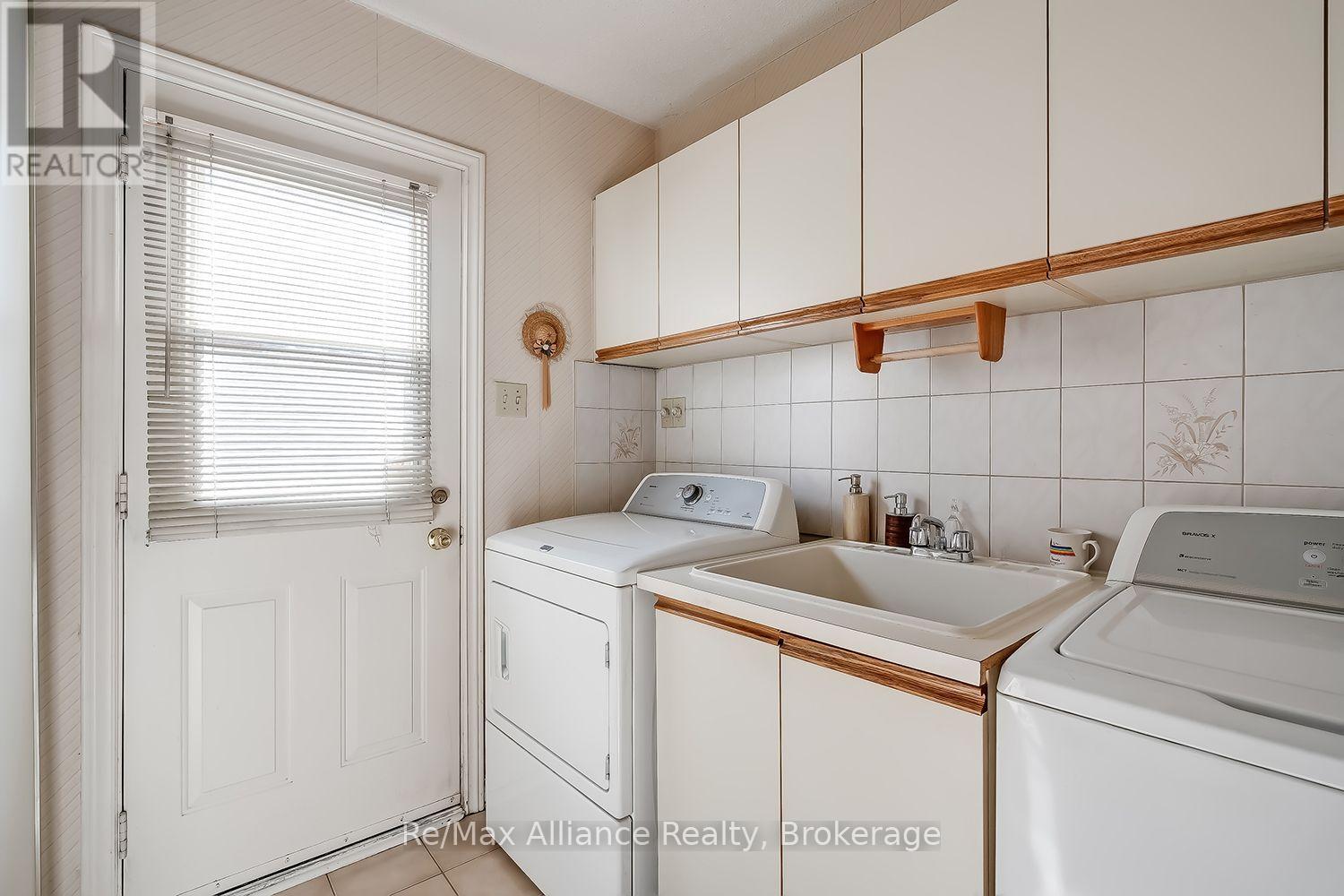 Laundry room with washer and dryer, utility sink, tiled backsplash, and white cabinets with wood trim.