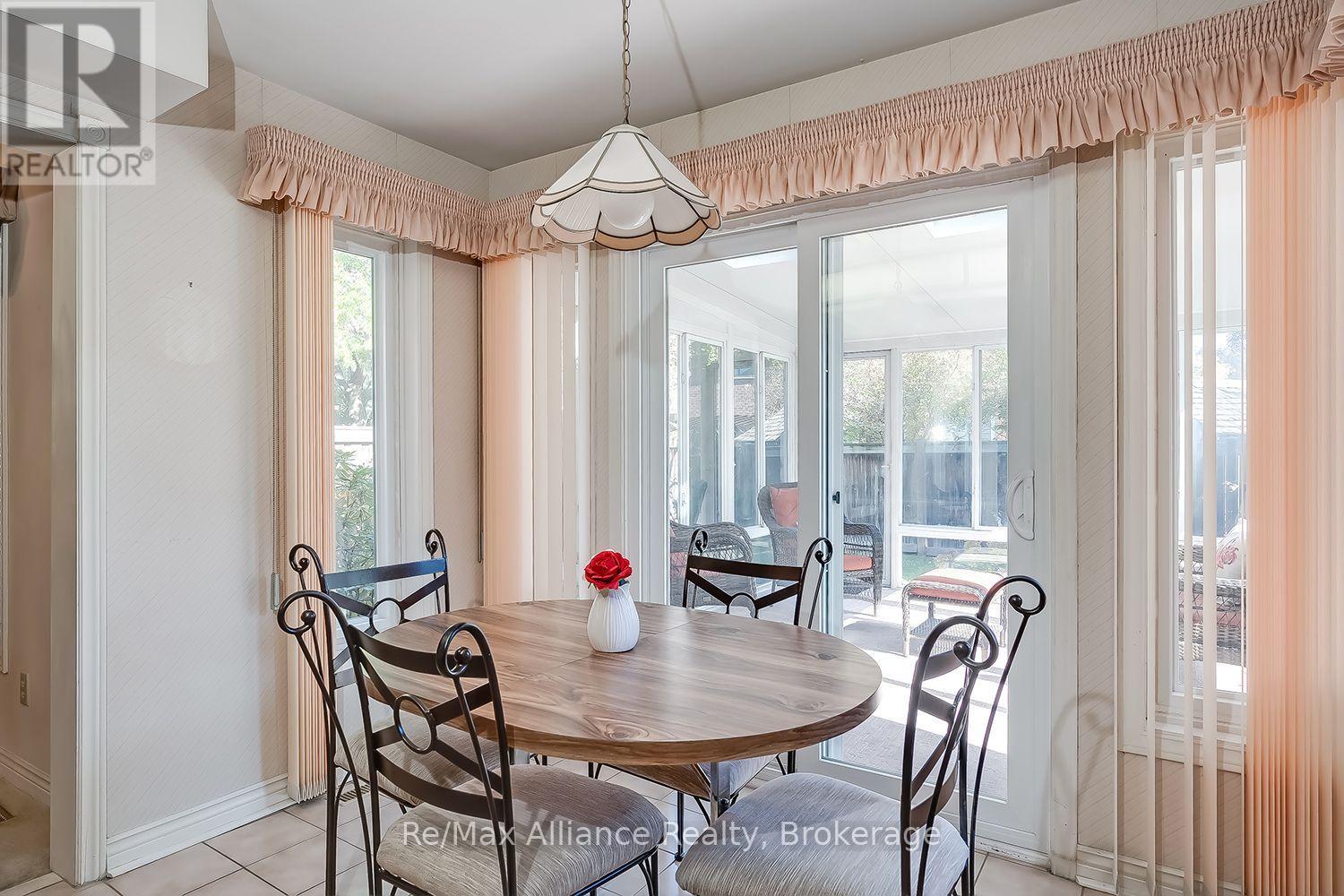 Dining area with an oval wood table, peach curtains, and glass doors to a sunroom.