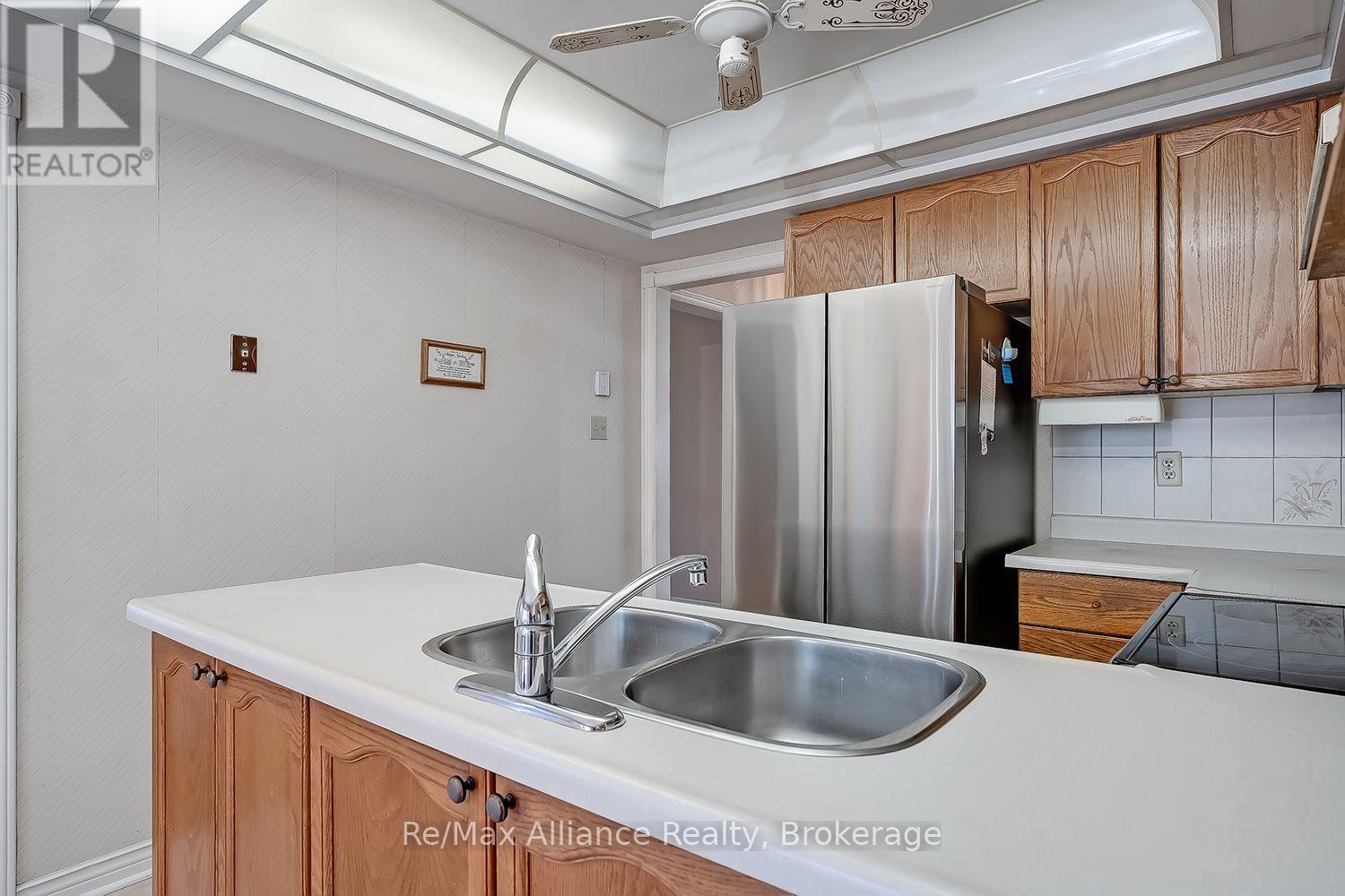 Kitchen with warm wood cabinets, a double sink peninsula, and stainless-steel refrigerator.