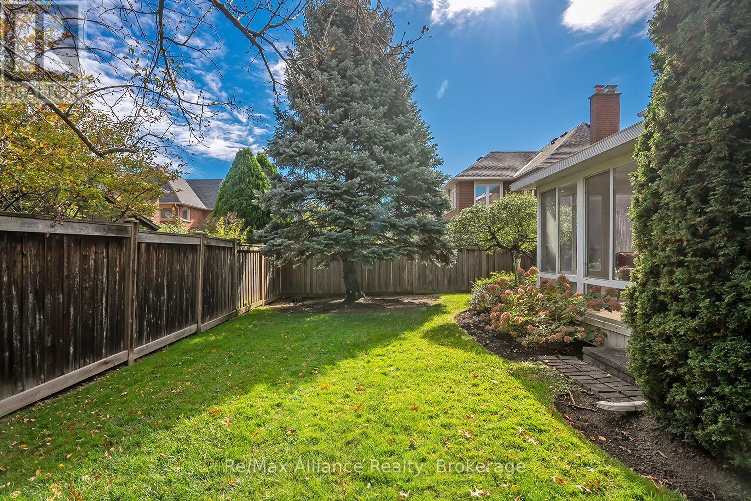 Fenced backyard with a green lawn, large spruce tree, and screened sunroom.