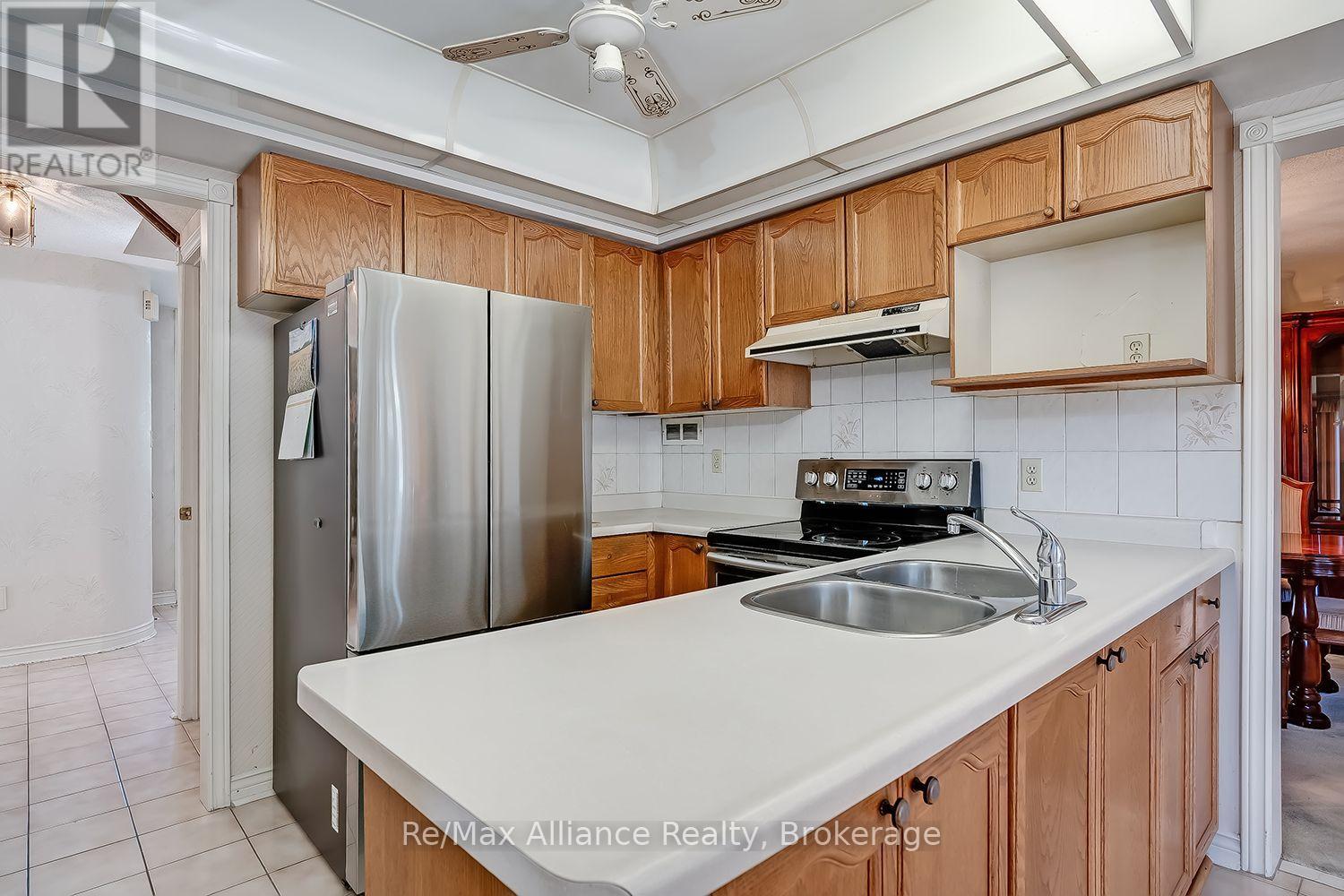Kitchen with honey-toned wood cabinets, a white peninsula and double sink, and stainless steel appliances.