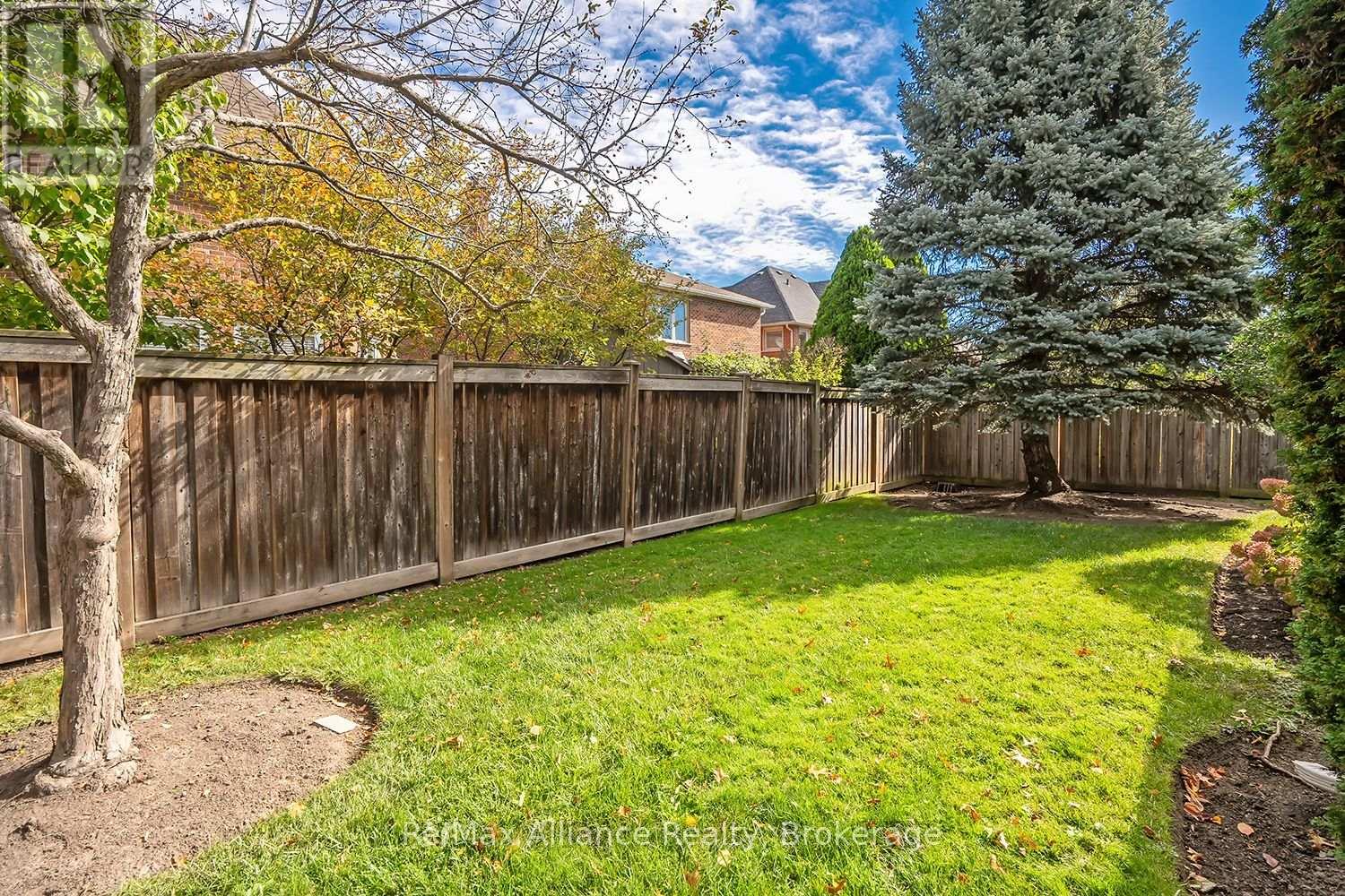 Fenced backyard with a green lawn, mature trees, and a large blue spruce.