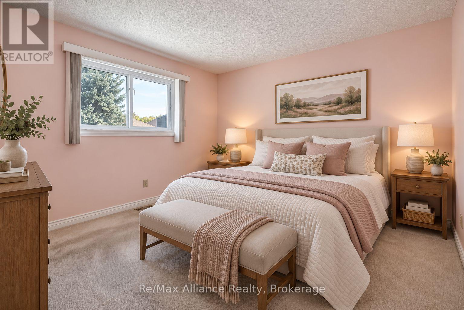 Staged bedroom with a white quilted bed, blush walls, and a window overlooking trees.