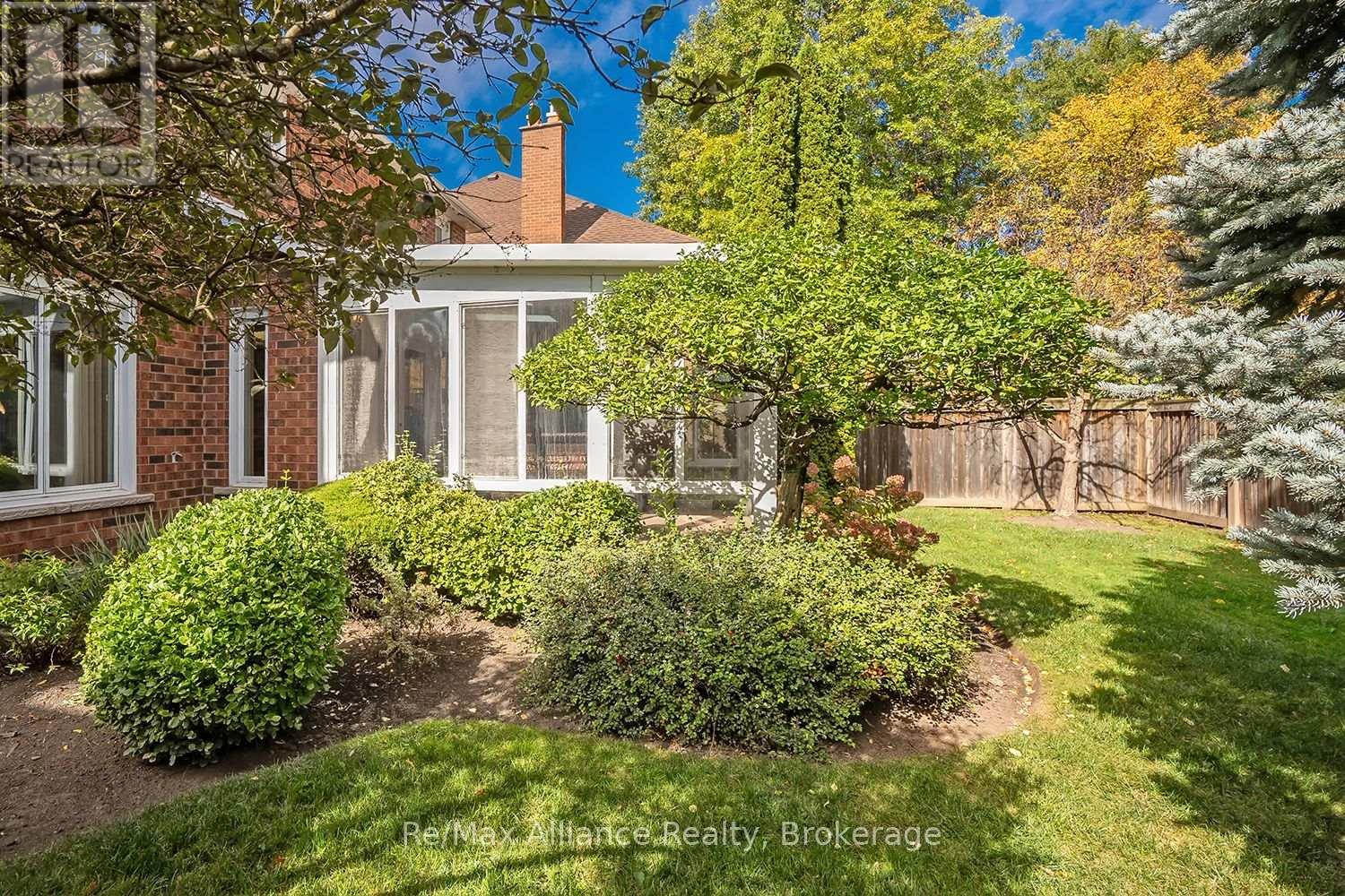 Brick house backyard with a white-framed sunroom, landscaped shrubs, lawn, and wooden privacy fence.