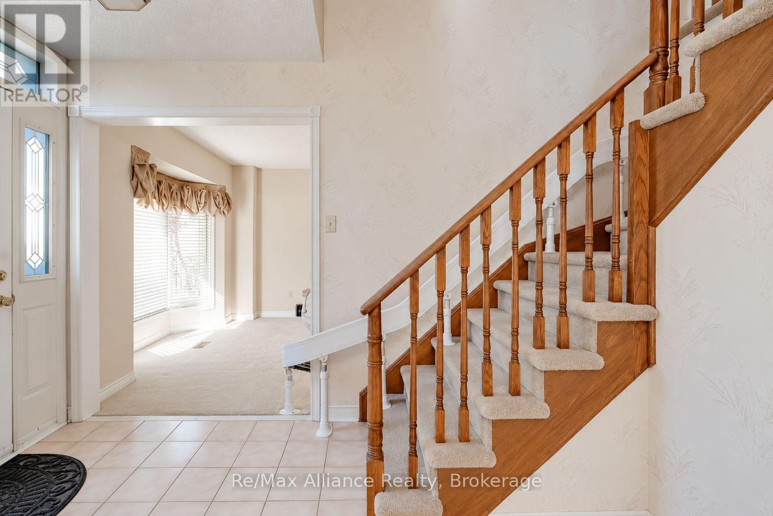 Foyer with a tiled floor, decorative-glass front door, and carpeted staircase with wooden railings.